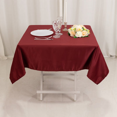 Burgundy tablecloth on a dining table with plates and floral centerpiece.
