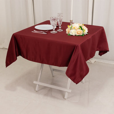 Burgundy tablecloth on a dining table set with flowers and glassware.