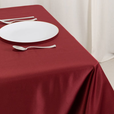 Red tablecloth with a white plate and silverware on a dining table.