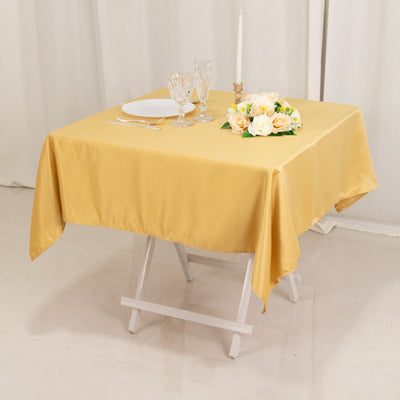 Yellow tablecloth draped over a table set for dining with flowers and glassware.
