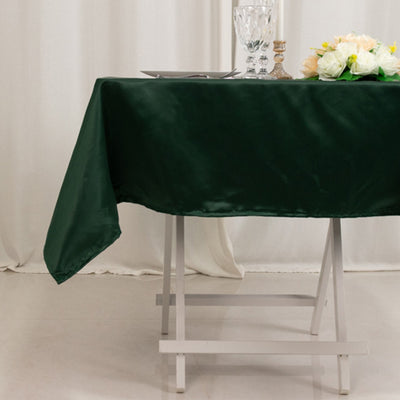 Green satin tablecloth draped over a white table with flowers and glassware.