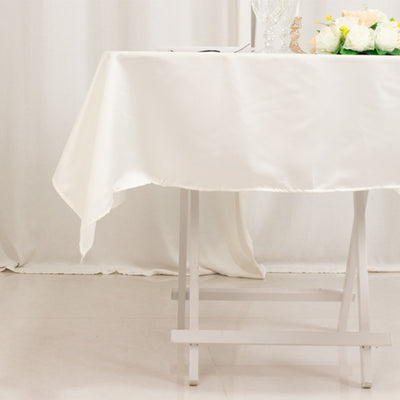 White tablecloth draped over a table with flowers and glasses on a plain backdrop.