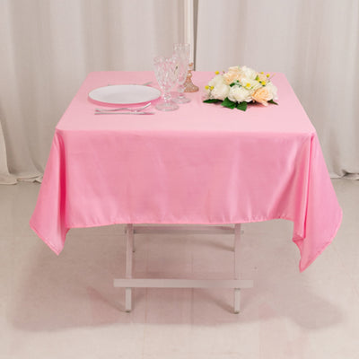 Pink satin tablecloth draped over a table with plates and flowers.