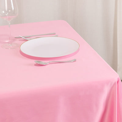 Pink tablecloth with white plate and silver cutlery on a dining table.