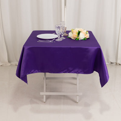 Purple tablecloth draped over a table with plates and glasses set for dining.