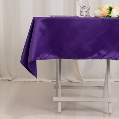Purple satin tablecloth draped on a table with decorative glassware and flowers.