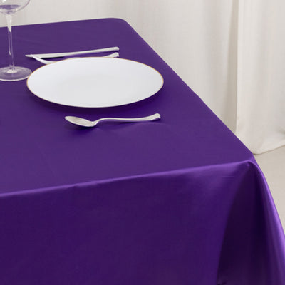Purple tablecloth draping a table set with a plate and silverware.