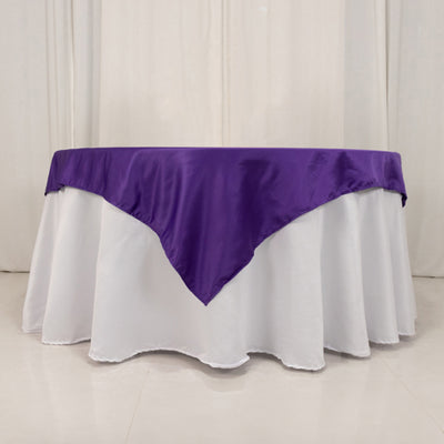Purple tablecloth draped over a round table with a white base.