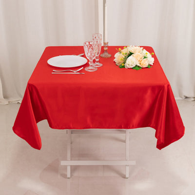 Red tablecloth draped over a table set with dinnerware and floral centerpiece.