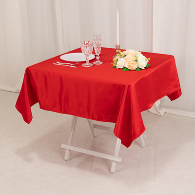 Red tablecloth draped over a table set with glasses, a plate, and a floral arrangement.