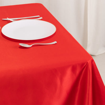 Red tablecloth with a white plate and silver cutlery on a table.