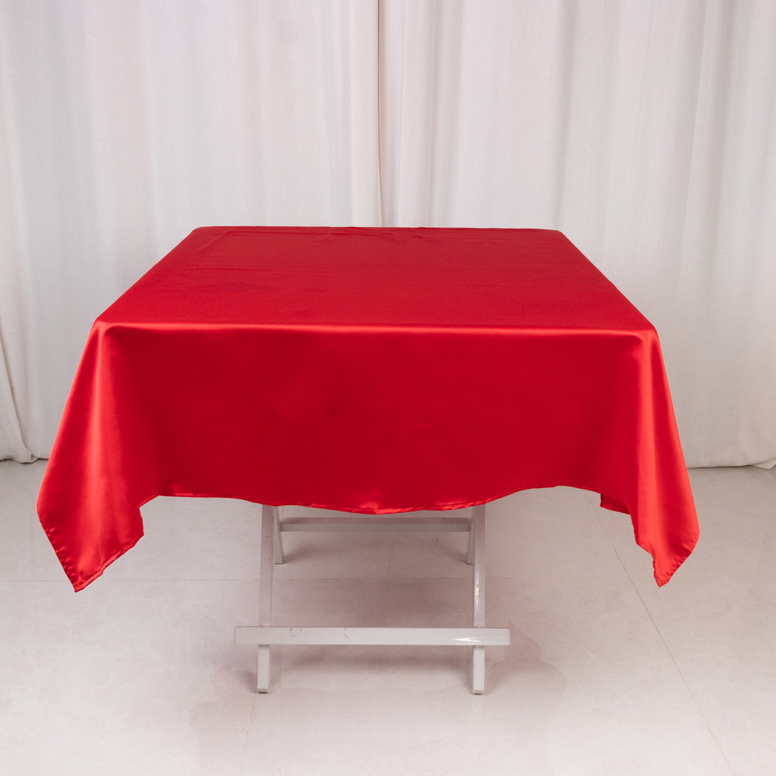Red satin tablecloth on a folding table with a plain background.
