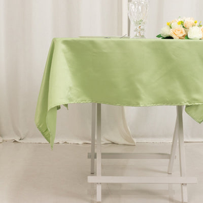 Green satin tablecloth draped over a white table with floral arrangement.