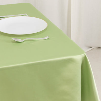 Green tablecloth with a white plate and silver spoon set on a table.