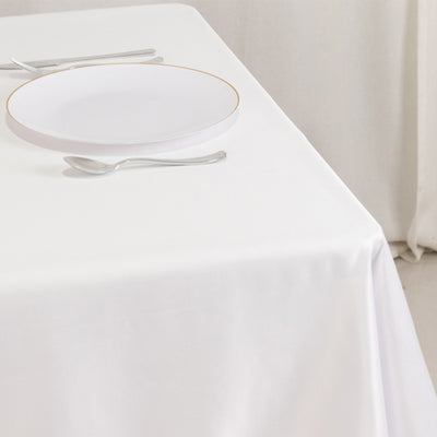 Elegant white table setting with a gold-rimmed plate and silver utensils.