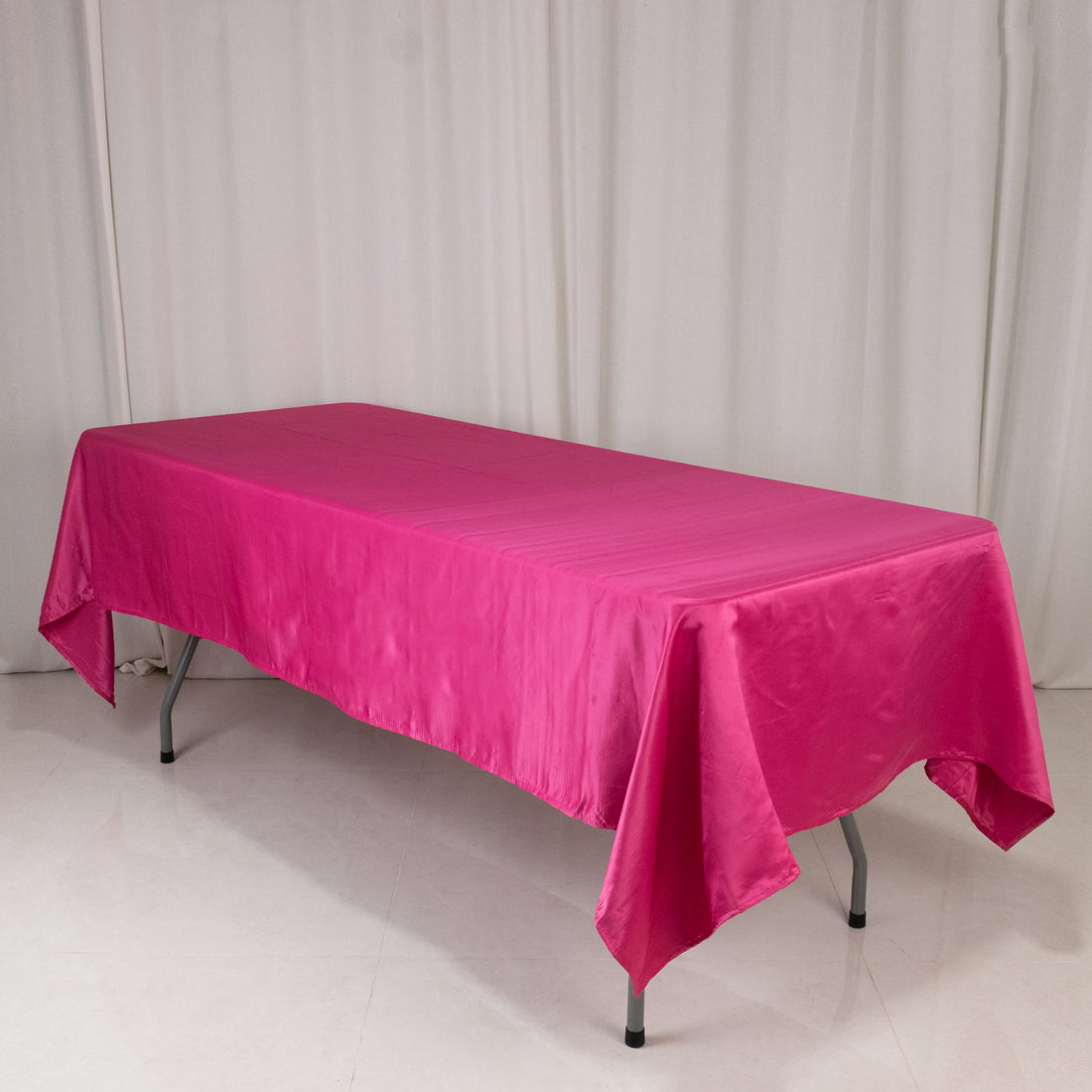 Pink satin tablecloth draped over a folding table in a studio setting.