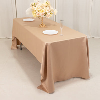 Elegant beige tablecloth draped over a table, decorated with flowers and tableware.
