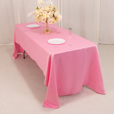 Pink tablecloth draped over a table with plates and a floral centerpiece.