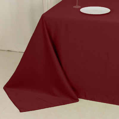 Burgundy tablecloth draped on a table with a plate and glass.