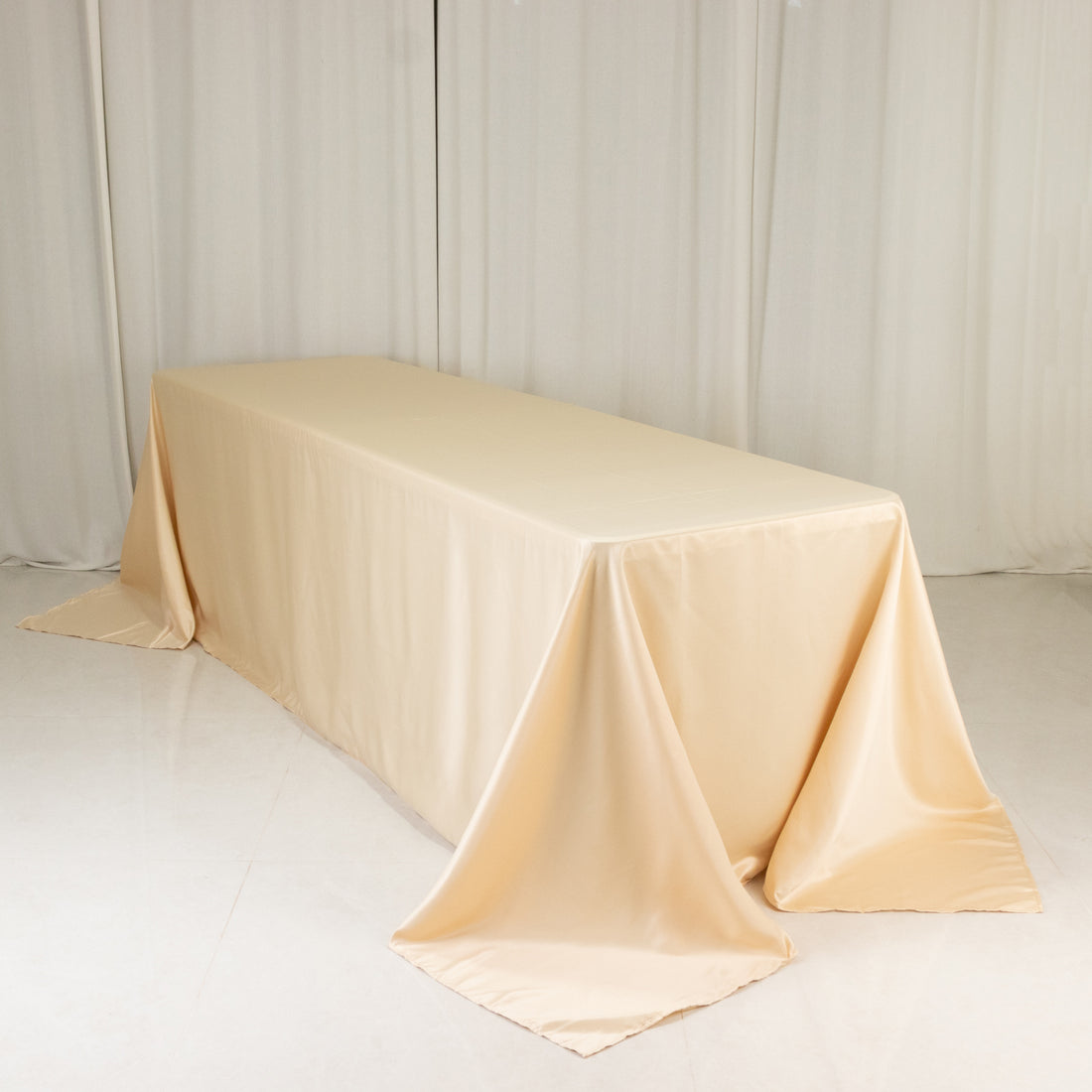 Beige satin tablecloth draped over a table in a studio setting.