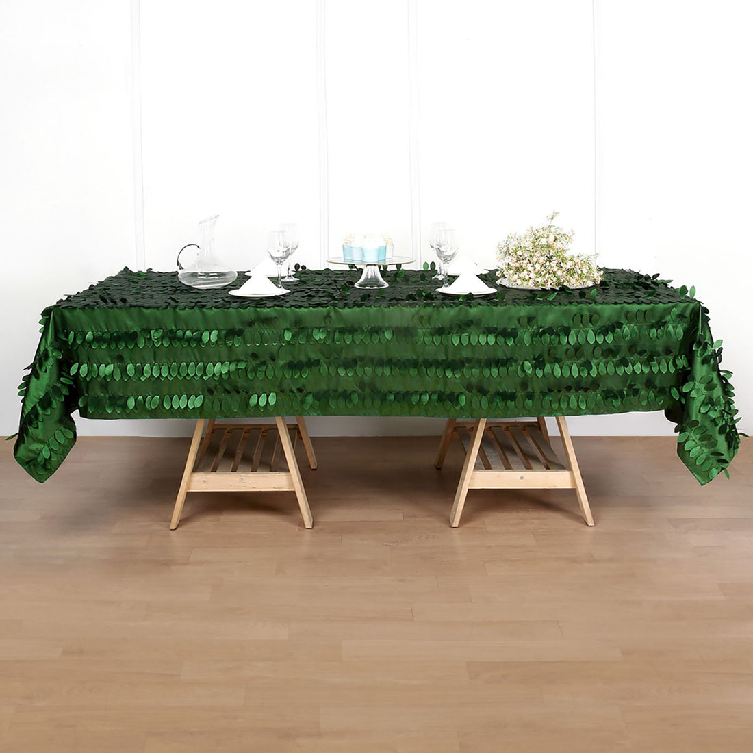 Green sequin tablecloth on a wooden table with glassware and floral accents.
