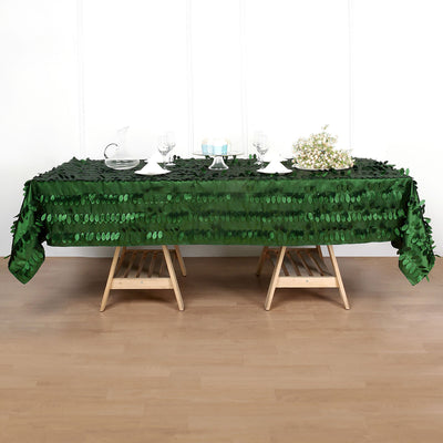 Green sequin tablecloth on a wooden table with glassware and floral accents.