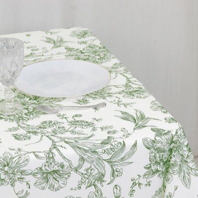 Floral green and white tablecloth with plate and glassware set on a table.
