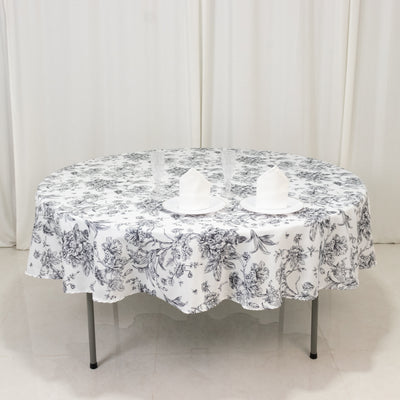 Round table with floral tablecloth and white napkins on a plain backdrop.