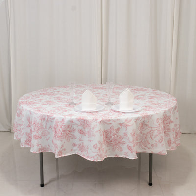 Round table with floral pink tablecloth and white candles on a plain backdrop.