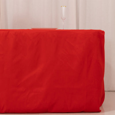 Red tablecloth draped over a table with a glass and plate on top.