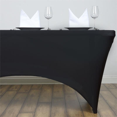 Black fitted tablecloth with white napkins and wine glasses on a wooden floor.