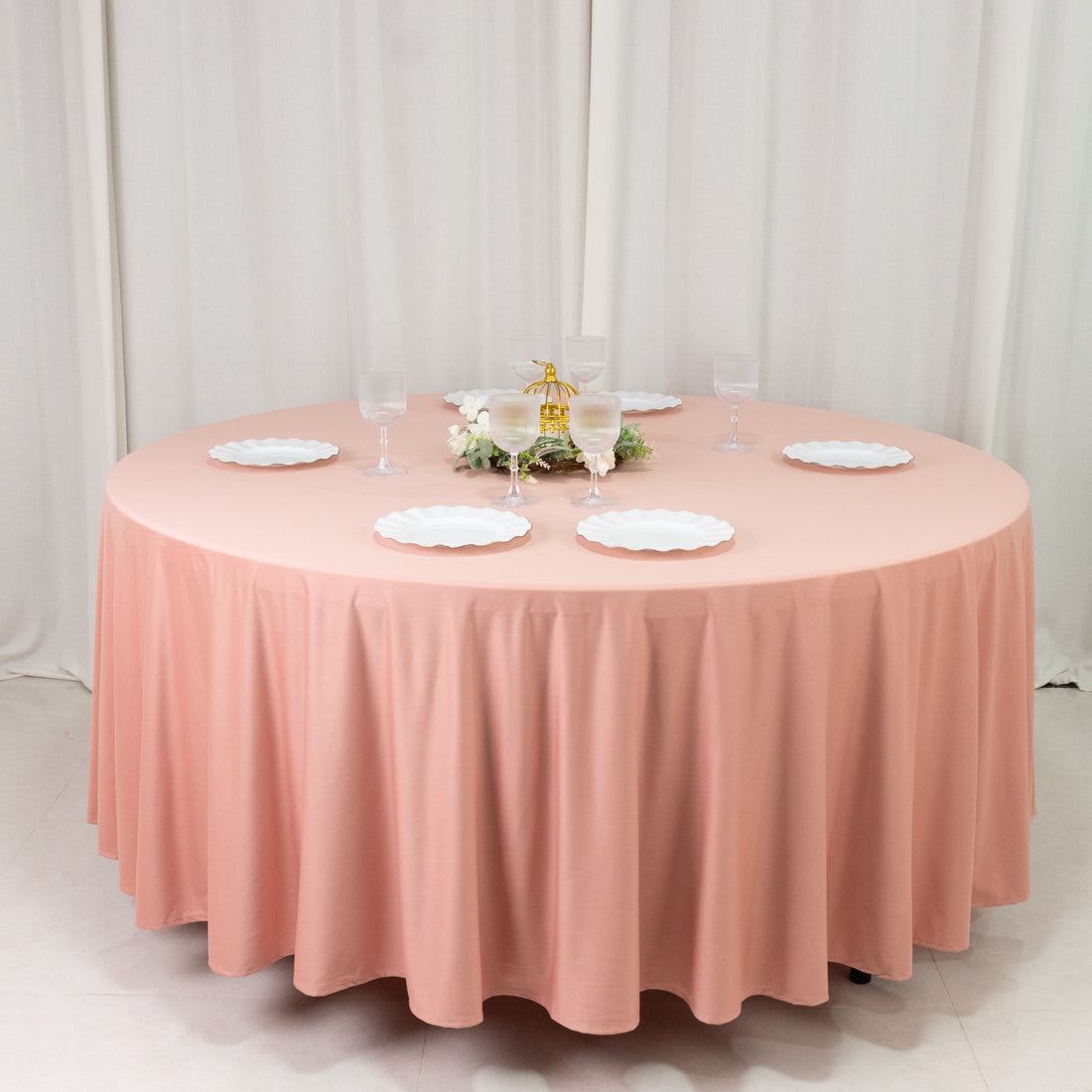 Round pink tablecloth draped over a circular table set for a meal.