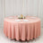 Round pink tablecloth draped over a circular table set for a meal.
