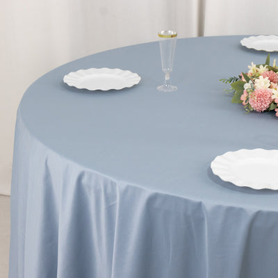 Blue tablecloth draped on a round table with white plates and floral centerpiece.
