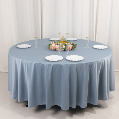 Round table set with blue tablecloth, plates, and floral centerpiece.