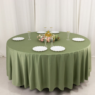 Round olive green tablecloth with white plates and decorative centerpiece.