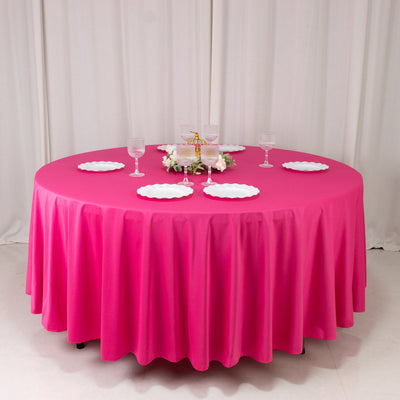Round pink tablecloth with white plates and glasses set for dining.