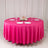 Round pink tablecloth with white plates and glasses set for dining.