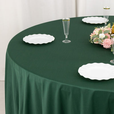 Green round tablecloth with white plates and floral centerpiece on a dining table.