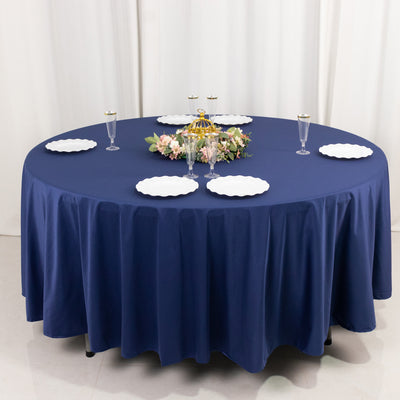 Round navy tablecloth with white plates and elegant centerpiece on a dining table.