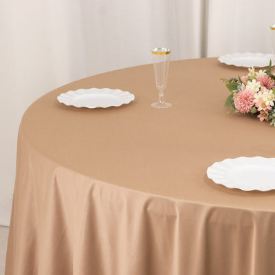 Round beige tablecloth draping over a table set with white plates and a floral centerpiece.