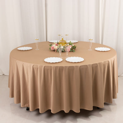 Elegant round table set with a beige tablecloth, plates, and floral centerpiece.