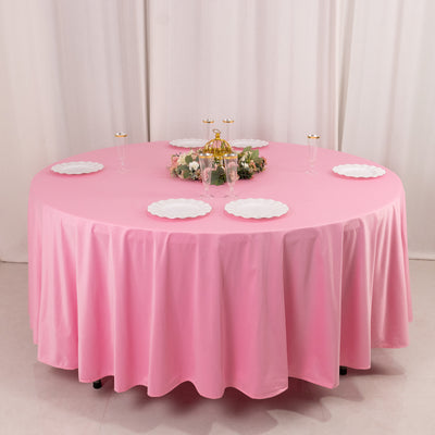Round pink tablecloth with white plates and a decorative centerpiece.