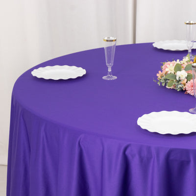 Purple tablecloth with white plates and floral arrangement on a round table.