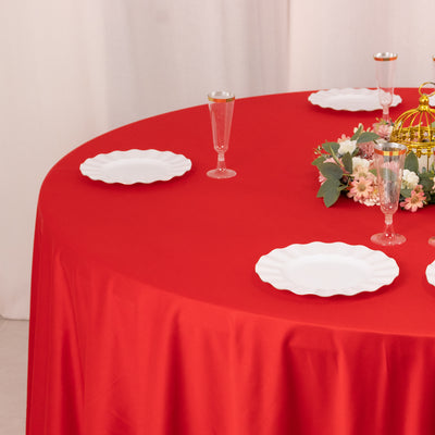 Red tablecloth with white plates and floral centerpiece on a round table.