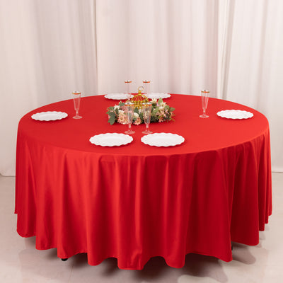 Red tablecloth draped over a round table with decorative plates and floral centerpiece.