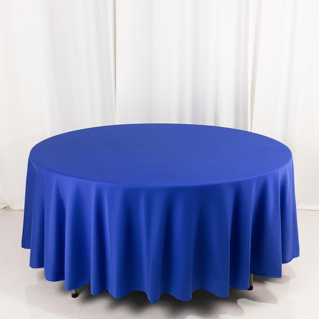 Blue round tablecloth with elegant draping on a white backdrop.