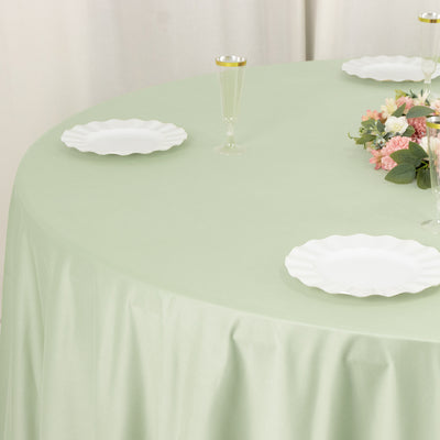 Green tablecloth with white plates and floral centerpiece on a round table.