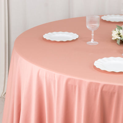 Round pink tablecloth with white plates and glassware on a dining table.