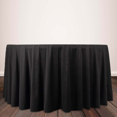 Black round tablecloth draped over a table on a wooden floor.